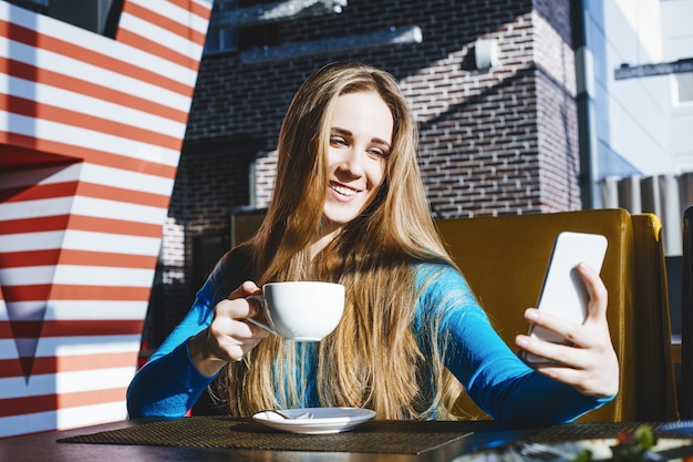 Mulher jovem e bonita moda de sucesso e linda com um telefone celular e uma xícara de café em um café