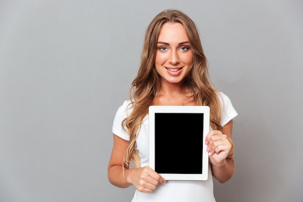 Mulher jovem e bonita mostrando computador tablet com tela em branco isolada em uma parede cinza