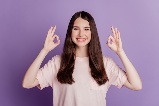 Mulher jovem e bonita mostrando sinal de ok com um sorriso dentuço na parede roxa