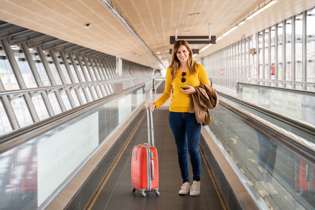 Mulher jovem e bonita muito feliz andando na esteira no aeroporto com sua bagagem