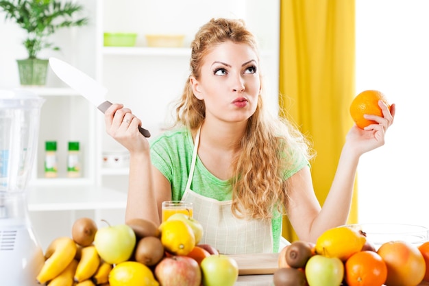 Mulher jovem e bonita na cozinha com laranja e faca.