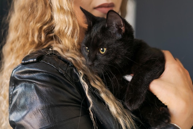 Mulher jovem e bonita na jaqueta de couro segura gato preto em seus braços perto dela