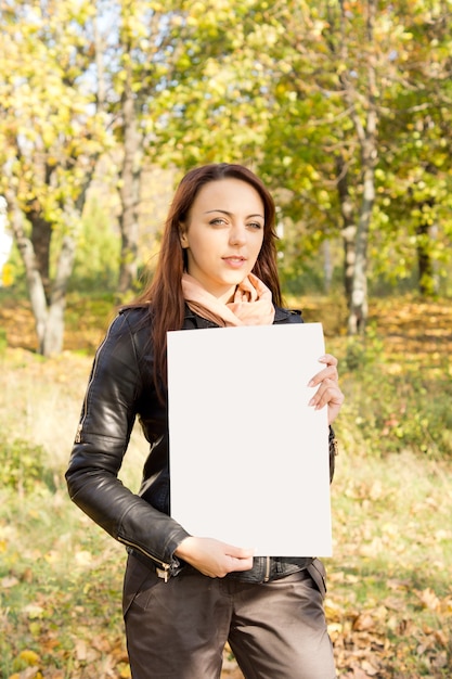 Mulher jovem e bonita na moda segurando um cartaz em branco para o seu texto nas mãos, ao ar livre