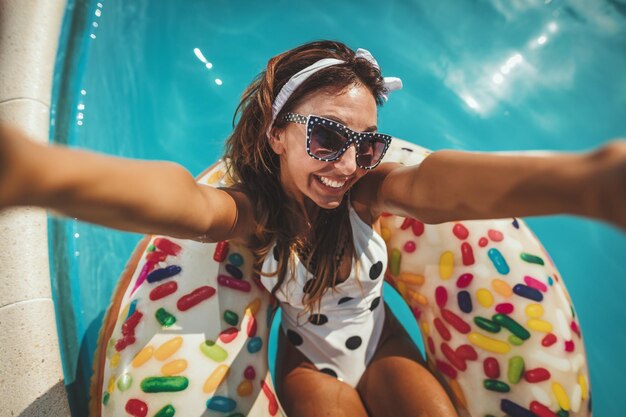 Mulher jovem e bonita na piscina nada no donut de anel inflável e se diverte fazendo selfie na água nas férias.