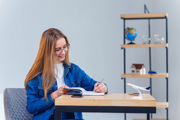 Mulher jovem e bonita no escritório vestindo roupas jeans, faça algumas anotações no caderno.