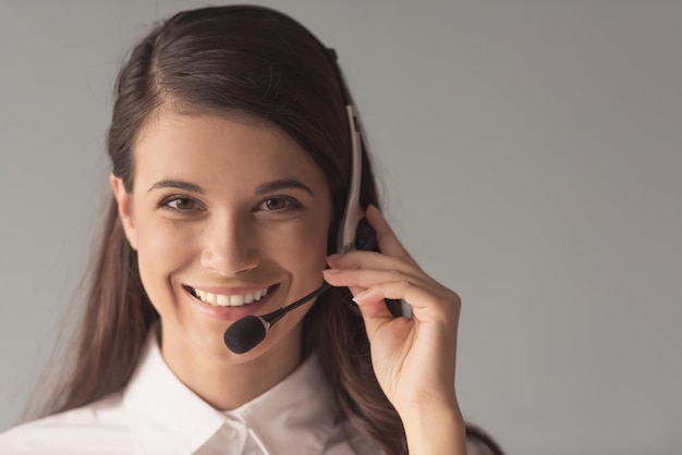 Mulher jovem e bonita no fone de ouvido está olhando para a câmera e sorrindo em fundo cinza