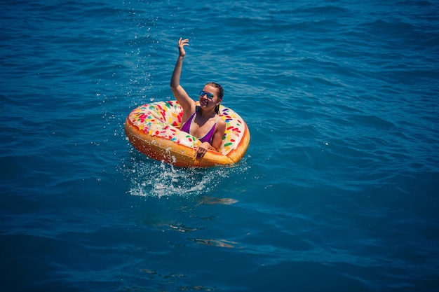 Mulher jovem e bonita no mar nada em um anel inflável e se diverte nas férias Garota em um maiô brilhante no mar sob a luz do sol