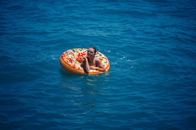 Mulher jovem e bonita no mar nada em um anel inflável e se diverte nas férias Garota em um maiô brilhante no mar sob a luz do sol