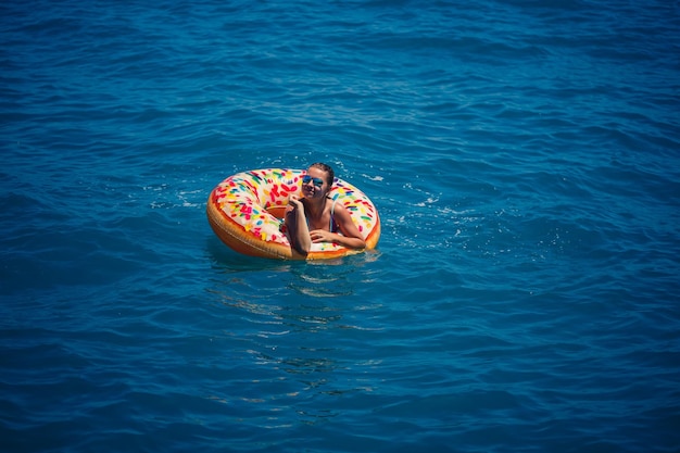 Mulher jovem e bonita no mar nada em um anel inflável e se diverte nas férias Garota em um maiô brilhante no mar sob a luz do sol