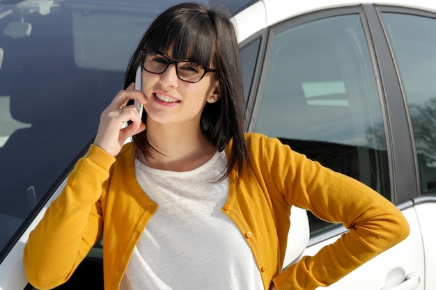 Mulher jovem e bonita no telefone contra o carro dela