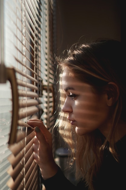 Mulher jovem e bonita olhando através das cortinas