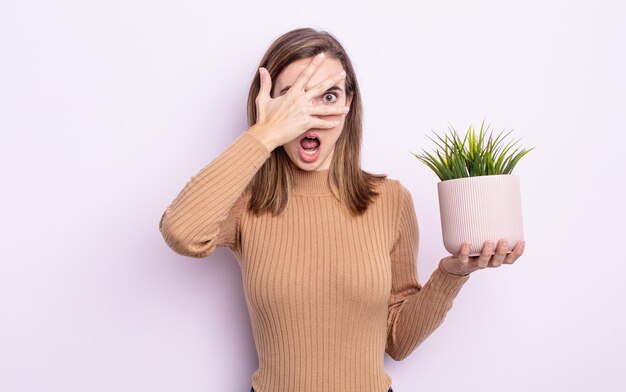 Mulher jovem e bonita olhando chocado, assustado ou aterrorizado, cobrindo o rosto com a mão. conceito de planta