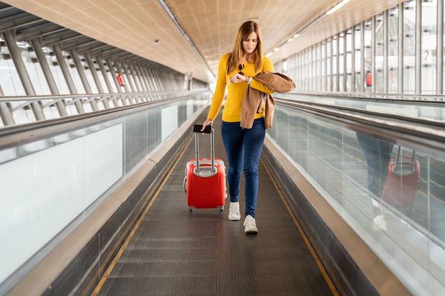 Mulher jovem e bonita olhando para o relógio no aeroporto ou estação com sua bagagem