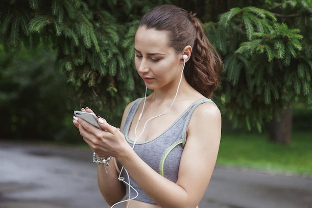 Mulher jovem e bonita ouvindo música enquanto corre pelo caminho em um parque verde