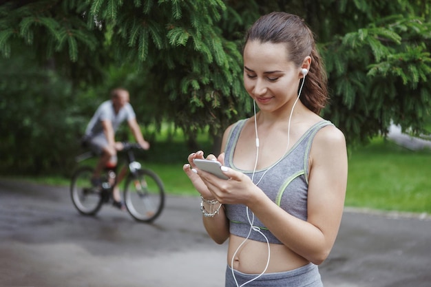 Mulher jovem e bonita ouvindo música enquanto corre pelo caminho em um parque verde