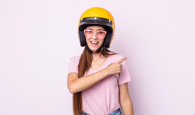 Mulher jovem e bonita parecendo animada e surpresa, apontando para o lado. piloto de moto e capacete