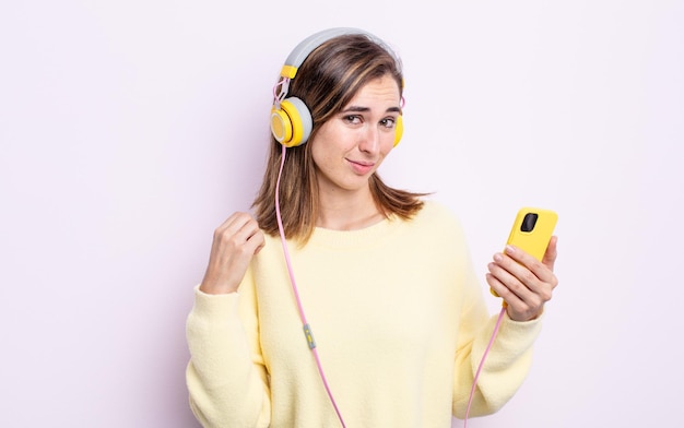 Mulher jovem e bonita parecendo arrogante, bem-sucedida, positiva e orgulhosa. fones de ouvido e conceito de telefone