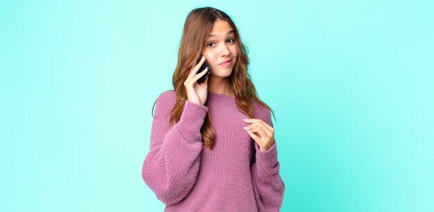 Mulher jovem e bonita parecendo arrogante, bem-sucedida, positiva e orgulhosa usando um smartphone