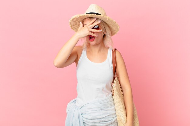 Mulher jovem e bonita parecendo chocada, assustada ou apavorada, cobrindo o rosto com a mão. conceito de turista de verão