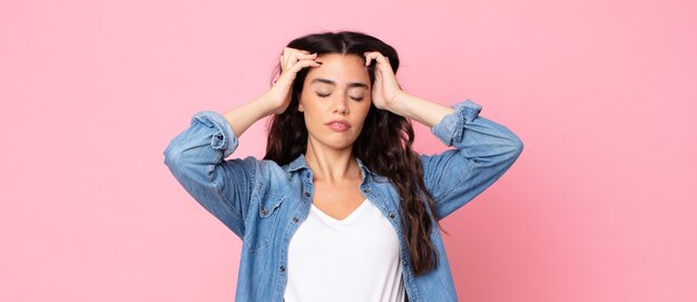 Mulher jovem e bonita parecendo concentrada, pensativa e inspirada, pensando e imaginando com as mãos na testa