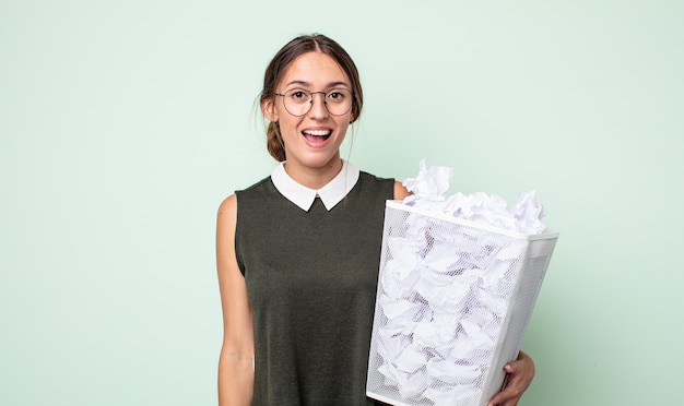 Foto mulher jovem e bonita parecendo feliz e agradavelmente surpresa. conceito de lixo de bolas de papel