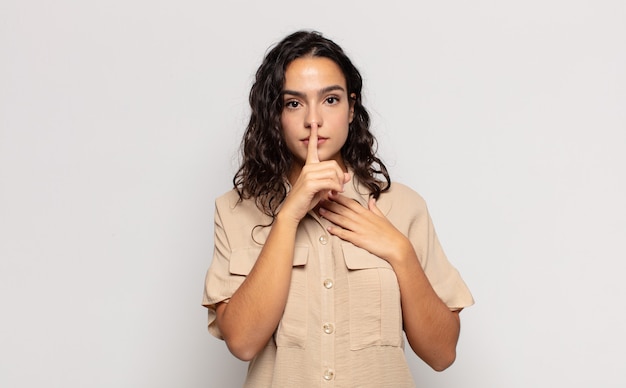 Foto mulher jovem e bonita parecendo séria e zangada com o dedo pressionado nos lábios exigindo silêncio ou silêncio, mantendo um segredo