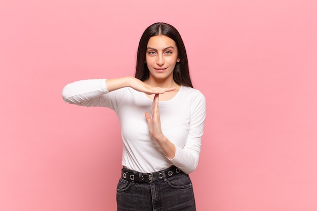 Mulher jovem e bonita parecendo séria, severa, zangada e descontente, fazendo sinal de castigo