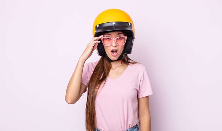 Foto mulher jovem e bonita parecendo surpresa, percebendo um novo pensamento, ideia ou conceito. motociclista e capacete