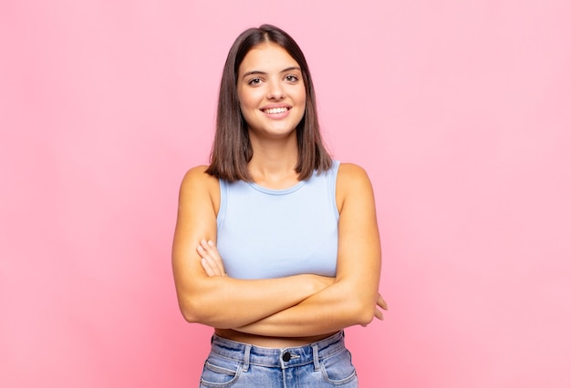 Mulher jovem e bonita parecendo uma empreendedora feliz, orgulhosa e satisfeita, sorrindo com os braços cruzados