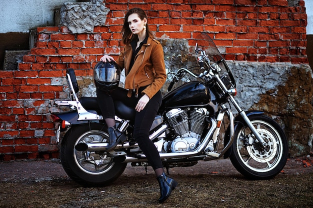 Mulher jovem e bonita posando com moto perto da parede de tijolos