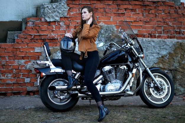 Mulher jovem e bonita posando com moto perto da parede de tijolos