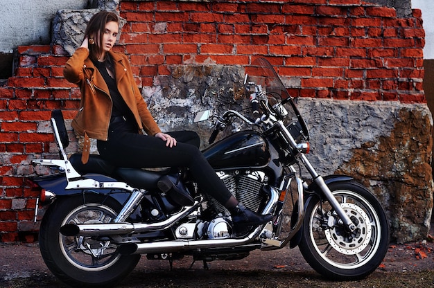 Mulher jovem e bonita posando com moto perto da parede de tijolos