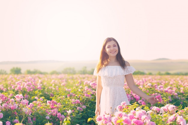 Mulher jovem e bonita posando perto de rosas em um jardim.