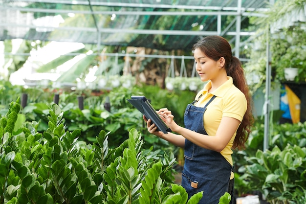 Mulher jovem e bonita positiva trabalhando no mercado de plantas e verificando o número de flores encomendadas