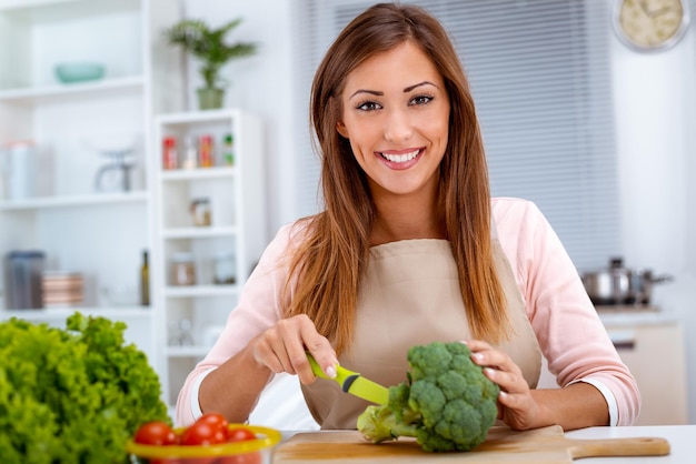 Mulher jovem e bonita preparando comida vegetariana na mesa da cozinha.