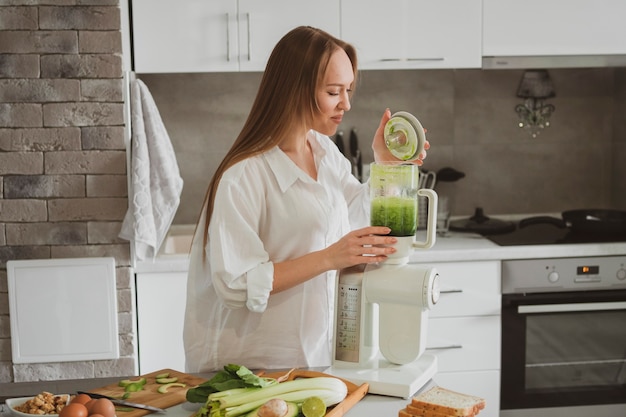 Mulher jovem e bonita preparando um smoothie verde saudável na cozinha