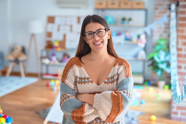 Mulher jovem e bonita professora sorrindo feliz e confiante. De pé com um sorriso no rosto no jardim de infância