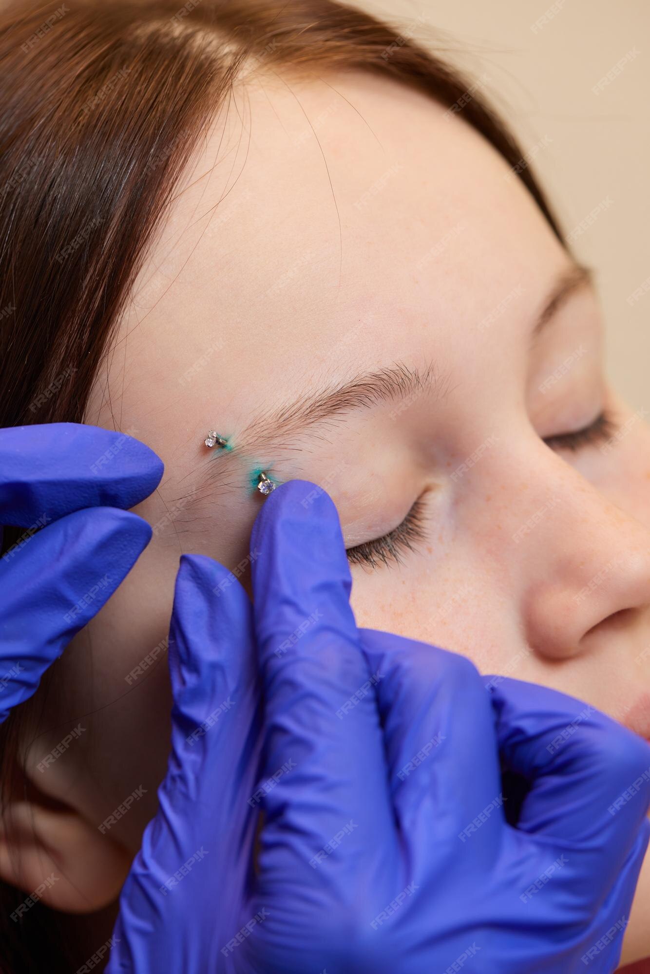 Mulher jovem e bonita recebendo seu piercing de sobrancelha com luvas azuis