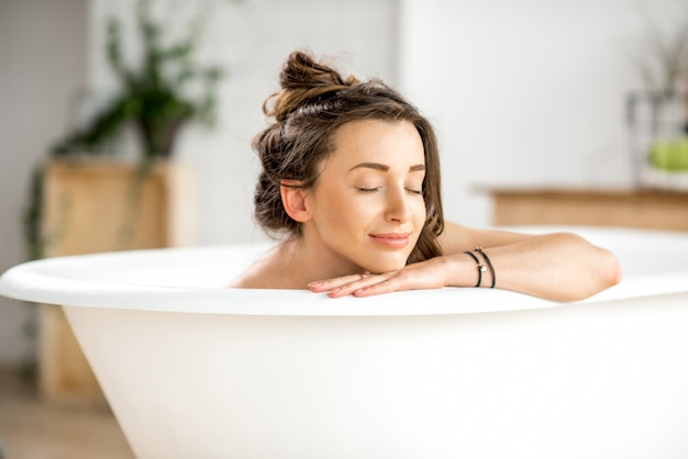 Mulher jovem e bonita relaxando deitada na banheira do banheiro