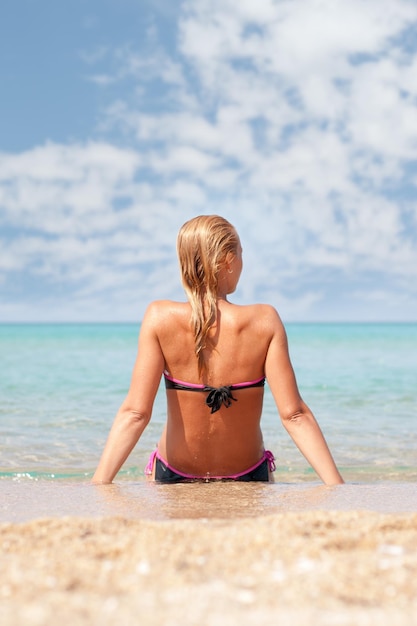 Mulher jovem e bonita relaxante na praia. Visão traseira.