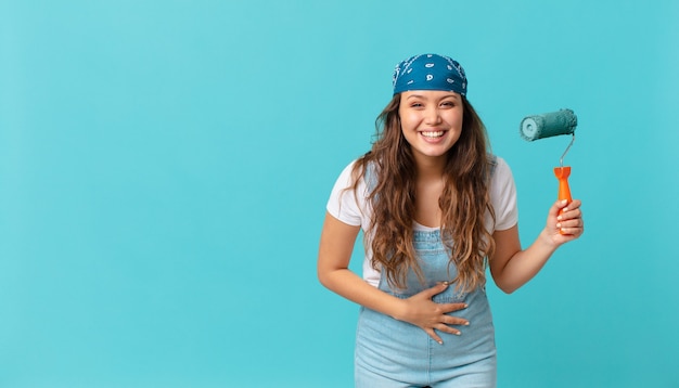 Mulher jovem e bonita rindo alto de uma piada hilária e pintando uma parede