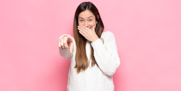 Mulher jovem e bonita rindo de você, apontando para a frente e tirando sarro ou zombando de você