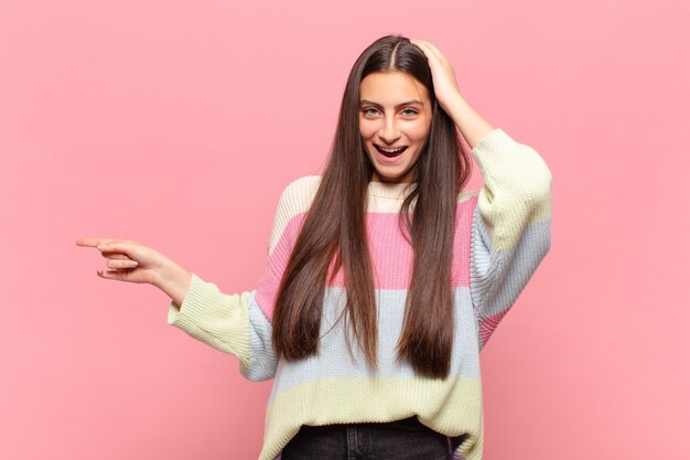 Mulher jovem e bonita rindo, parecendo feliz, positiva e surpresa, percebendo uma ótima ideia apontando para o espaço lateral da cópia