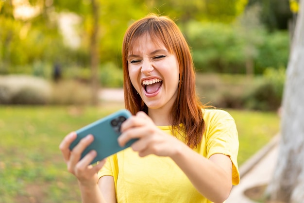 Mulher jovem e bonita ruiva ao ar livre brincando com o celular