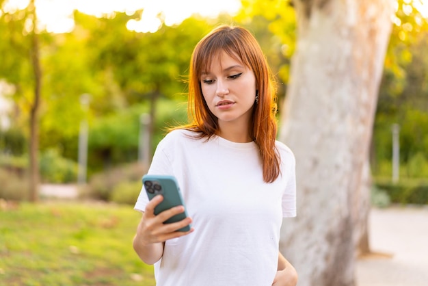Mulher jovem e bonita ruiva ao ar livre usando telefone celular