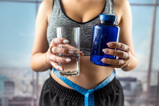 Mulher jovem e bonita saudável segurando um copo de água para pedir vitaminas para perda de peso mãos com um copo de vitaminas de água para perda de peso