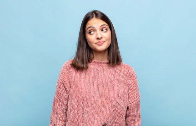 Mulher jovem e bonita se perguntando, tendo ideias e pensamentos felizes, sonhando acordada, olhando para copiar o espaço ao lado