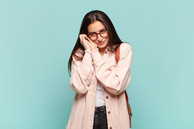 Mulher jovem e bonita se sentindo apaixonada e bonita, adorável e feliz, sorrindo romanticamente com as mãos ao lado do rosto. conceito de estudante