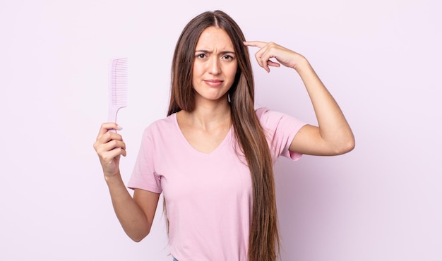 Mulher jovem e bonita se sentindo confusa e confusa, mostrando que você é louco. conceito de pente de cabelo