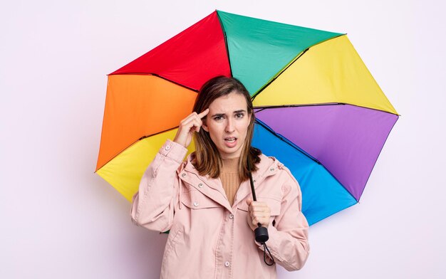 Mulher jovem e bonita se sentindo confusa e perplexa, mostrando que você é louco. conceito de guarda-chuva